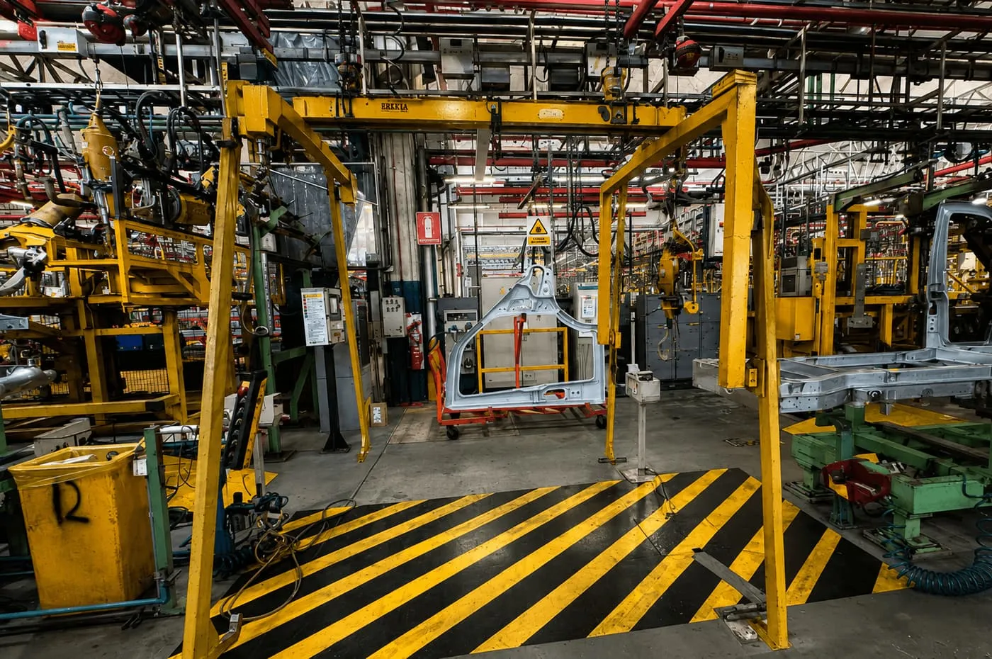 Pórtico metálico amarillo con panel de carrocería suspendido en línea de producción automotriz
