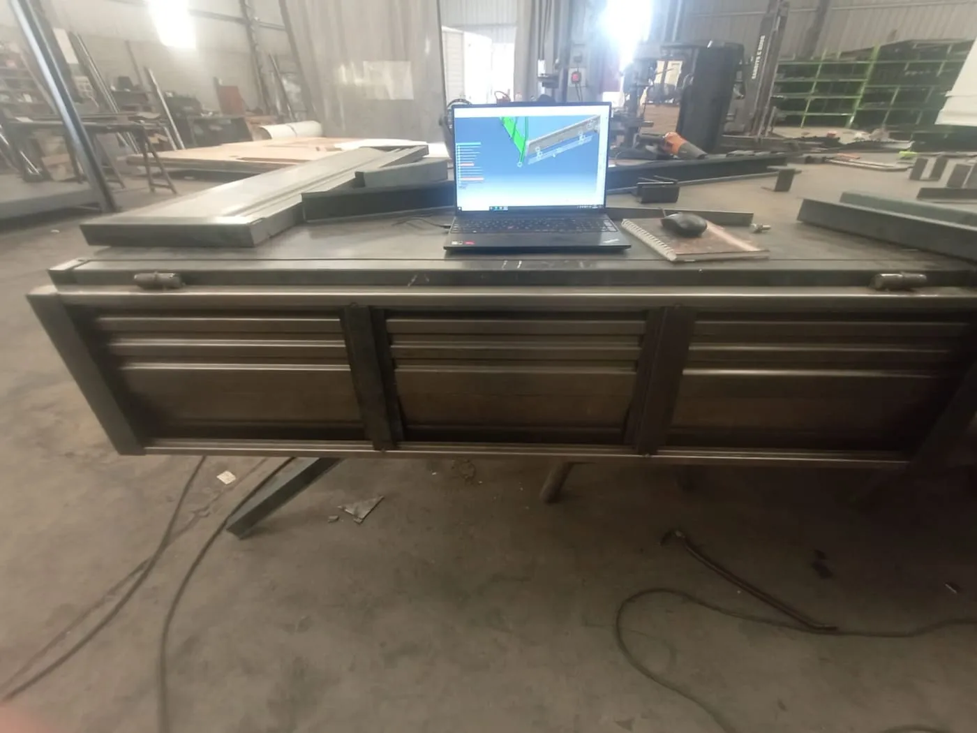 Baranda metálica de carrocería sobre banco de taller junto a notebook con modelo CAD