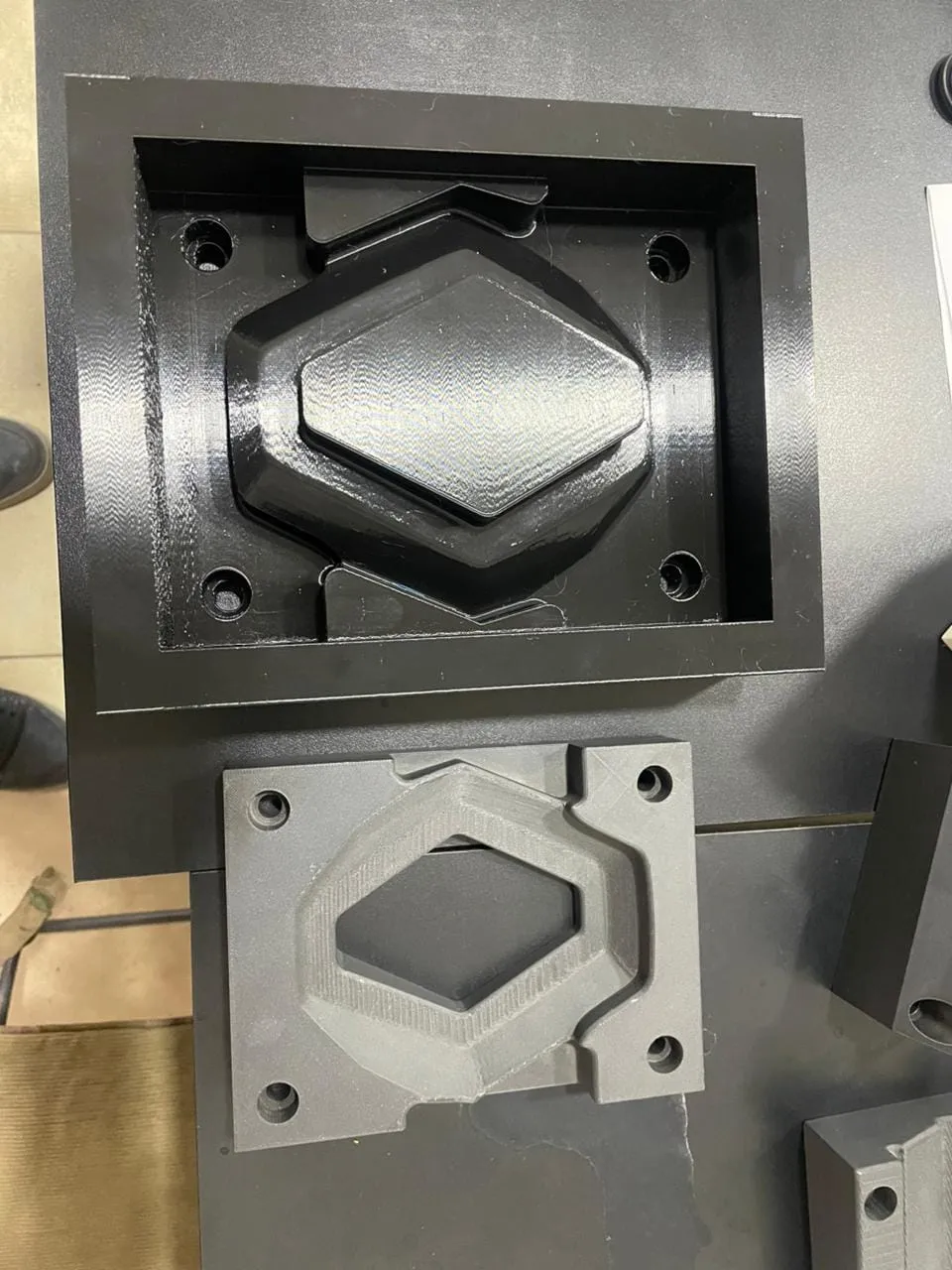 Moldes impresos en 3D con capas visibles, cavidad hexagonal en negro y gris sobre mesa de taller