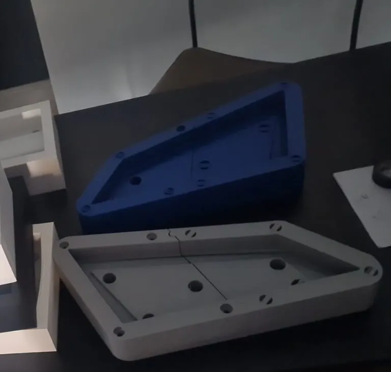 Piezas impresas en 3D azul y gris con alojamientos y perforaciones, terminadas sobre mesa