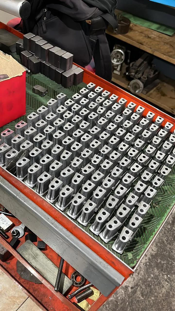 Serie de piezas metálicas mecanizadas con perforaciones alineadas sobre carro de taller