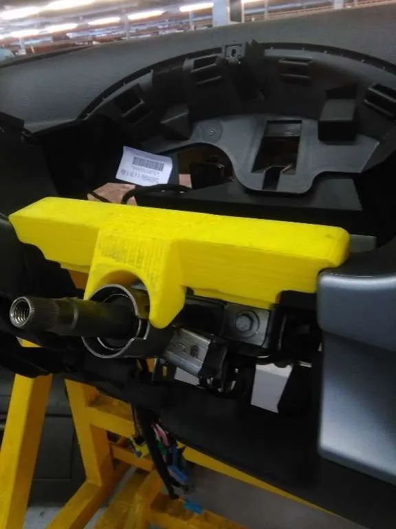 Pieza impresa en 3D en PLA amarillo montada sobre el tablero de un vehículo en línea de producción